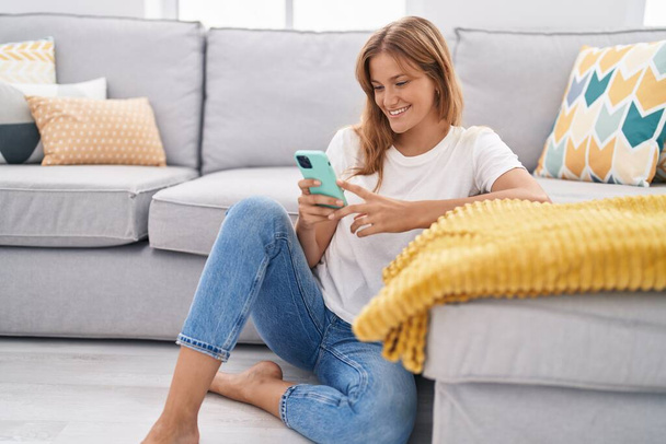 Jovem loira usando smartphone sentado no chão em casa - Foto, Imagem