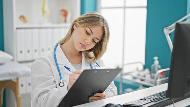 Молодая блондинка-врач пишет на планшете, думая в клинике - Фото, изображение