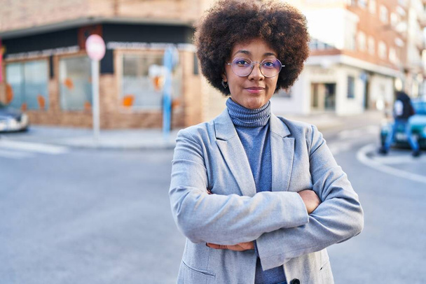 Africano americano mulher executivo sorrindo confiante em pé com braços cruzados gesto na rua - Foto, Imagem