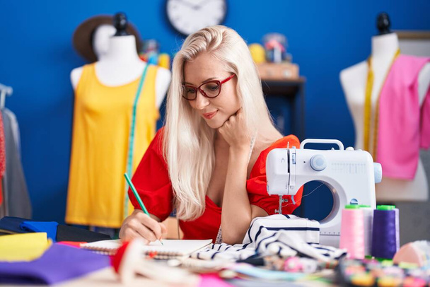 Jeune femme blonde tailleur souriant dessin confiant sur ordinateur portable au studio de couture - Photo, image