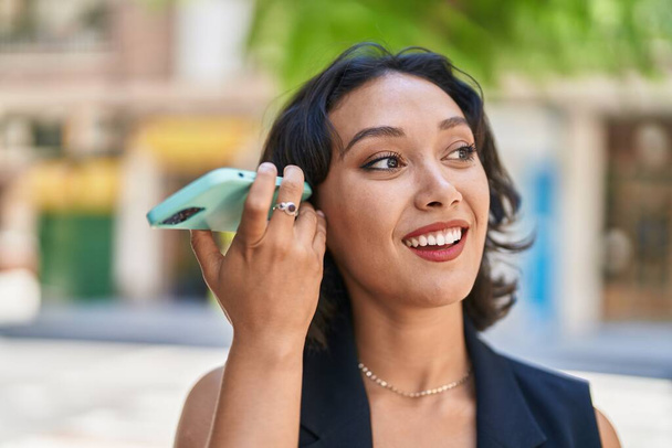 若い美しいヒスパニック系の女性は通りでスマートフォンによって自信を持ってリスニング音声メッセージを笑います - 写真・画像
