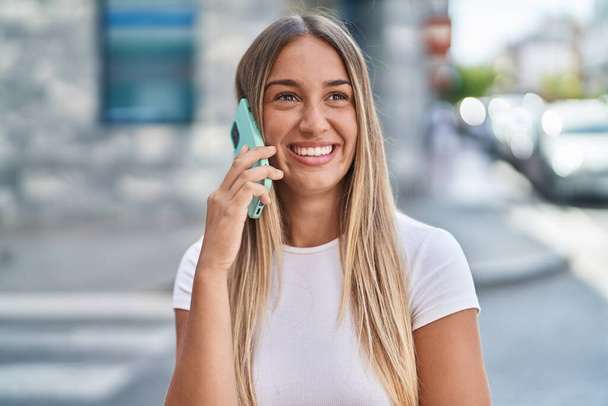 Fiatal gyönyörű spanyol nő mosolyog magabiztos beszél az okostelefonon az utcán - Fotó, kép