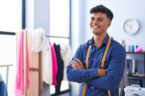 Молодий іспаномовний чоловік, посміхаючись впевнений, що стоїть з обіймами перетнув жест на фабриці одягу
 - Фото, зображення