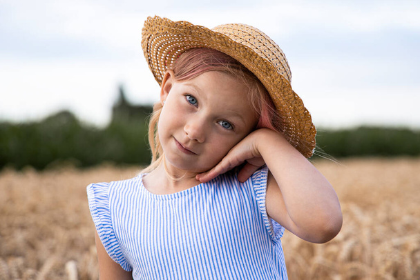 Cute child little girl in a hat on a background of a wheat field. - Photo, Image