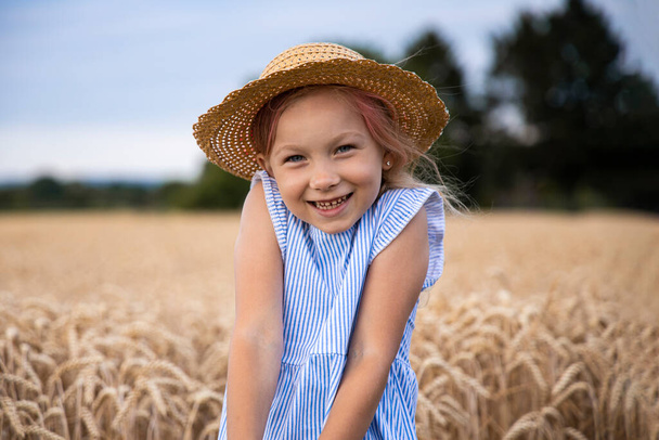 Nettes kleines Mädchen mit Hut auf dem Hintergrund eines Weizenfeldes. - Foto, Bild