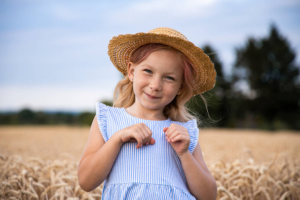 Милая маленькая девочка в шляпе на фоне пшеничного поля. - Фото, изображение