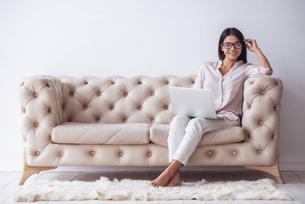 Otthoni iroda. Sikeres fiatal gyönyörű nő ül a nappaliban a kanapén, és használ laptop. - Fotó, kép