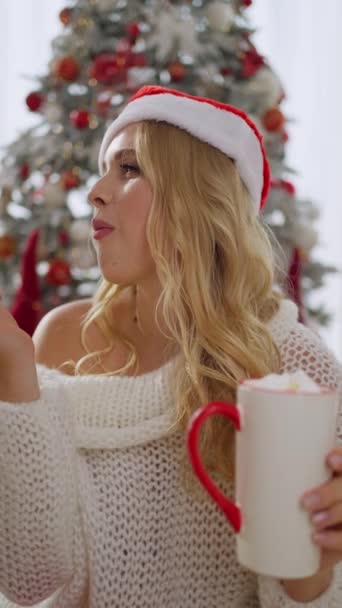 Een mooi meisje in een kerstmuts brengt tijd door thuis luisterend naar muziek en zoet gebak etend, genietend van een rust. - Video