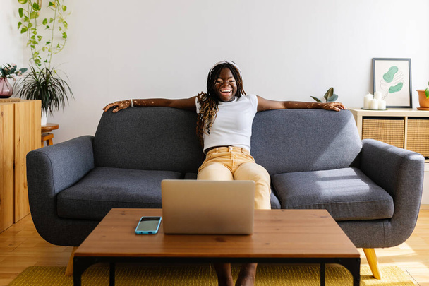 Młoda Afrykanka bawiąca się oglądając filmy online na laptopie w domu. Technologia i koncepcja stylu życia domowego. - Zdjęcie, obraz