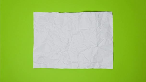 Video Top view of wrinkled textured white or light gray paper on bright green table. White crumpled paper texture background. Wrinkled, abstract paper background - Footage, Video