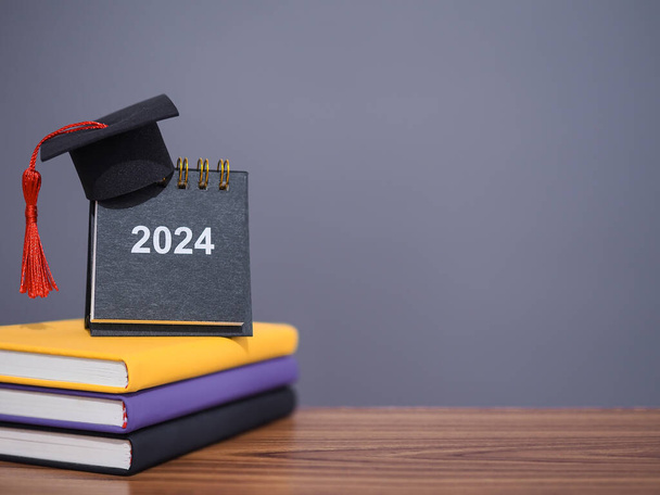 Cele studiów, 2024 Kalendarz biurko z kapeluszem ukończenia szkoły na kolorowe twardej książki. Koncepcja rozdzielczości, celu, działania, planowania i zarządzania czasem do ukończenia studiów w Nowym Roku 2024 - Zdjęcie, obraz