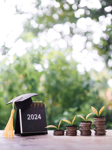 Objetivos do estudo, 2024 Calendário de mesa com chapéu de graduação e plantas crescendo na pilha de moedas. O conceito de poupar dinheiro para a educação, empréstimo estudantil, bolsa de estudos, propinas no Ano Novo 2024 - Foto, Imagem
