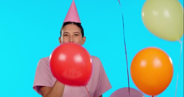 Birthday, happy and balloons with a nurse woman in studio isolated on a blue background for a celebration event. Portrait, healthcare and a young female medicine professional blowing a party horn. - Footage, Video