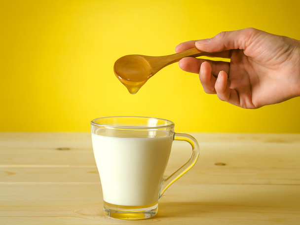 Miele che cade da cucchiaio in un bicchiere di latte
 - Foto, immagini