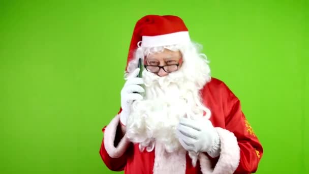 Hiteles örömteli Mikulás szemüvegben beszél az okostelefonján és gesztikulál. Vidám Mikulás piros ruhában karácsonykor. Zöld vászon. Kroma kulcs. - Felvétel, videó
