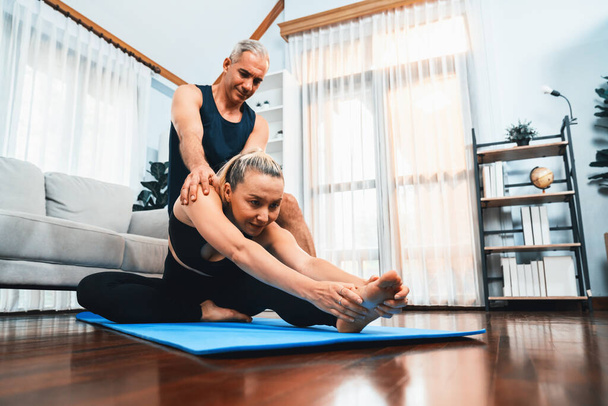 Gelukkig actief senior paar in sportkleding wordt ondersteunende en helpen op yoga houding samen thuis. Gezonde senioren man en vrouw levensstijl met yoga oefening. Klok - Foto, afbeelding
