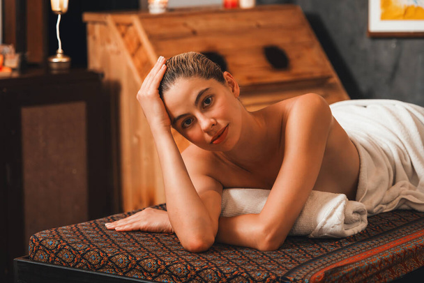 Красива молода жінка лежить на спа-ліжку перед дерев'яним шафою для сауни. Привабливі розслабляючі білі жінки в білому рушнику дивляться на камеру в очікуванні масажу тіла в сауні.. - Фото, зображення