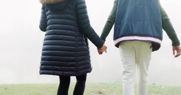 Couple, holding hands and walking in misty fog, travel or adventure together in the nature outdoors. Rear view of man and woman exploring natural environment in winter weather on holiday trip outside. - Felvétel, videó
