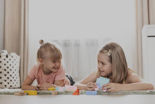 Dzieci bawiące się kolorowymi zabawkami. Dzieci siedzące na dywanie w domowej sypialni lub przedszkolu. Rozwój zdolności motorycznych, wyobraźnia, logiczne myślenie. Edukacyjne gry przyjazne dla środowiska - Zdjęcie, obraz