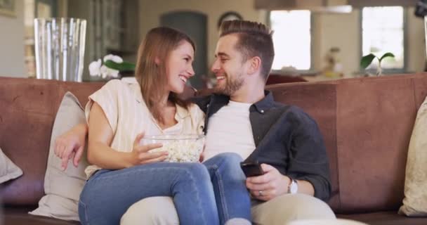 Happy couple, sofa and popcorn for romantic movies, comedy or watching tv together in home living room. Man, woman and comic television show on lounge couch with eating snack, relax or bond with love. - Imágenes, Vídeo