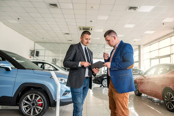 Modern araba galerisinde genç ve güzel bir müşteri erkek satıcısıyla el sıkışıyor, başarı anlaşması. satın alma aracı konsepti - Fotoğraf, Görsel