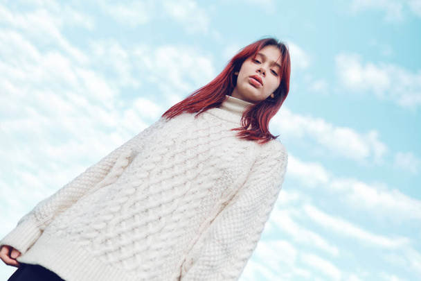 Teenage girl in a white sweater against the sky looks down at the camera. Low angle view. - Fotó, kép