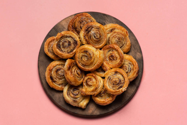 Vers gebakken zoete en krokante kaneelbroodjes. Op een houten plaat en roze ondergrond - Foto, afbeelding