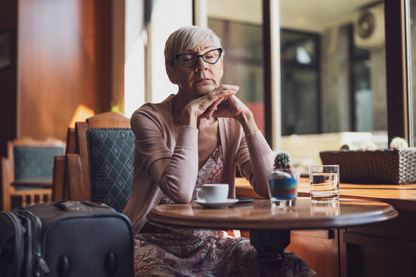 Idős nő ül egy kávézóban a repülőtéren, várja a beszállást.. - Fotó, kép