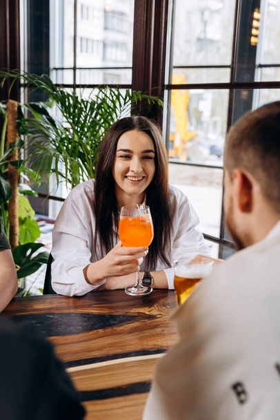 Young smiling woman enjoying a coctail in bar restaurant during rest with friends - Photo, Image
