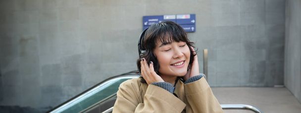 Portrait of happy woman, korean girl in headphones, listening music in headphones, enjoying sound of earphones, laughing and smiling. - Foto, Imagem