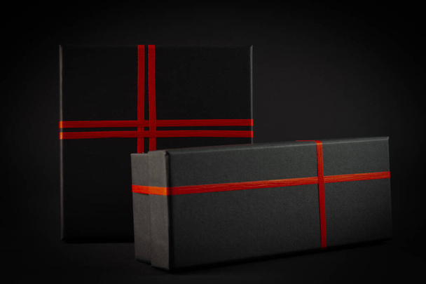 Černá dárková krabice s červenou stuhou luk na černém pozadí. Dárkový koncept. - Fotografie, Obrázek