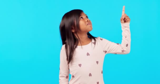 Маленькая девочка, смотрит и указывает на рекламу, стоящую на фоне синей студии. Женщина, ребенок или ребенок указывают пальцем на уведомление, рекламу или жест на макете. - Кадры, видео