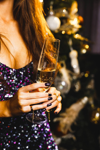 シャンパンのガラスでクリスマスツリーの近くに輝く青いドレスで華やかな白人女性の肖像画.新年とクリスマスのコンセプト - 写真・画像