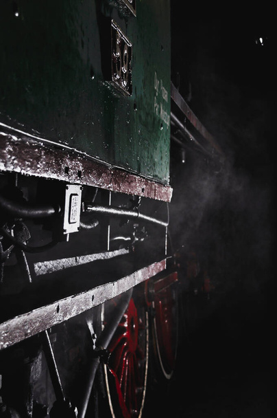 Kırmızı tekerlekleri olan antika yeşil bir tren vagonuna yakın çekim, karanlıkta loş ışık, dünyevi gece. - Fotoğraf, Görsel