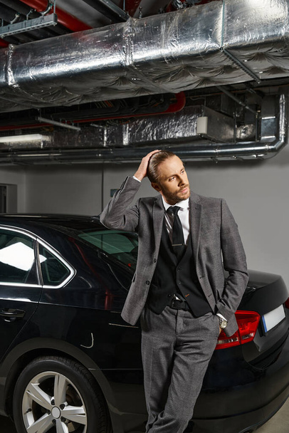 schöner Profi im eleganten schicken Anzug posiert in der Nähe seines Autos auf einem Parkplatz und schaut weg - Foto, Bild