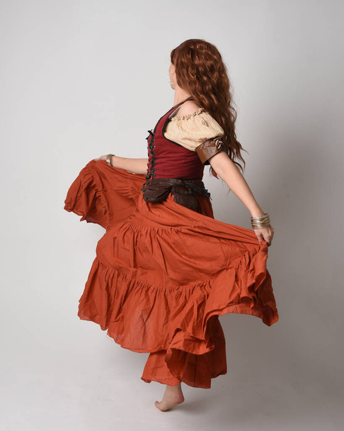 Полный портрет красивой рыжеволосой женщины в средневековой девичьей одежде, костюм гадалки. Стоя поза вид сзади, уходя. изолированные на студийном фоне. - Фото, изображение