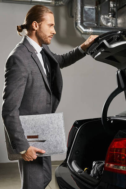 vertikale Aufnahme eines gutaussehenden Mannes mit Pferdeschwanz im gepflegten Anzug, der den Kofferraum seines Autos schließt, Geschäftskonzept - Foto, Bild