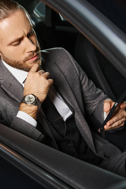 κάθετη βολή του όμορφου άνδρα σε κομψό κοστούμι με τηλέφωνο πίσω από το τιμόνι, επιχειρηματική ιδέα - Φωτογραφία, εικόνα