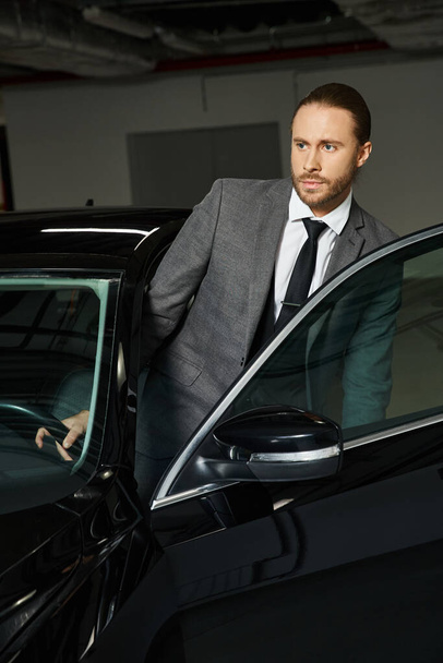 εμφανίσιμος επαγγελματίας με κομψό και έξυπνο κοστούμι μπαίνει στο αυτοκίνητό του στο πάρκινγκ, επιχείρηση - Φωτογραφία, εικόνα
