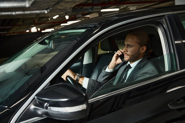 привлекательный элегантный профессионал в шикарном костюме разговаривает по телефону за рулем, бизнес-концепция - Фото, изображение