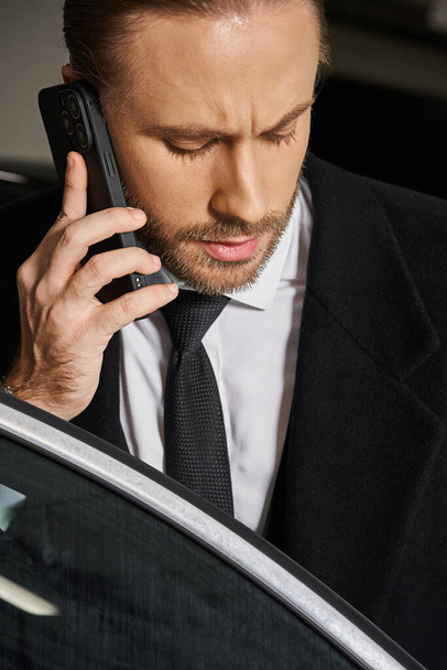 pionowe zdjęcie przystojnego biznesmena z rudymi włosami i brodą rozmawiającego przez telefon komórkowy w pobliżu samochodu - Zdjęcie, obraz