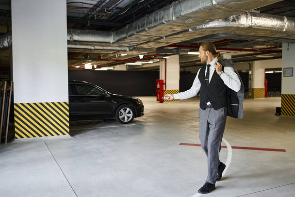 Aansprekende man met paardenstaart en baard met behulp van de sleutel op zijn auto op de parkeerplaats, business concept - Foto, afbeelding