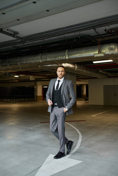 ansprechender stylischer Geschäftsmann im grau-eleganten Anzug posiert mit der Hand in der Tasche und blickt in die Kamera - Foto, Bild