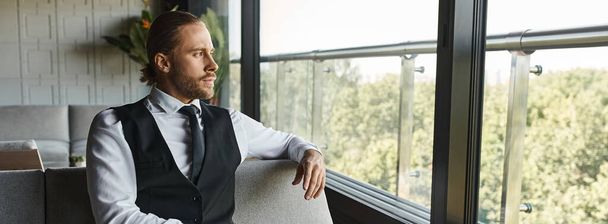 ελκυστικός άνδρας με έξυπνη στολή κάθεται στον καναπέ και κοιτάζοντας έξω από το παράθυρο, επιχειρηματική ιδέα, πανό - Φωτογραφία, εικόνα