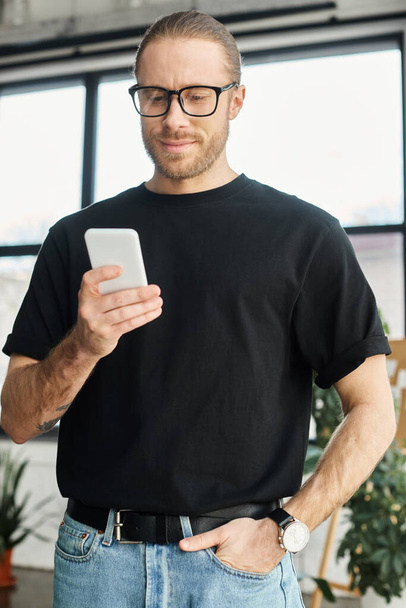 スマートフォンでポケットチャットで手で眼鏡と黒のTシャツで笑顔のビジネスマン - 写真・画像