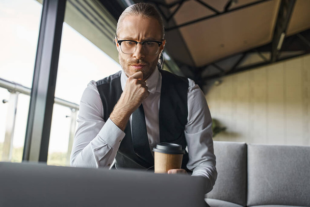 doordachte man in slimme kledij werkt aan zijn laptop met koffiebeker in de hand, business concept - Foto, afbeelding