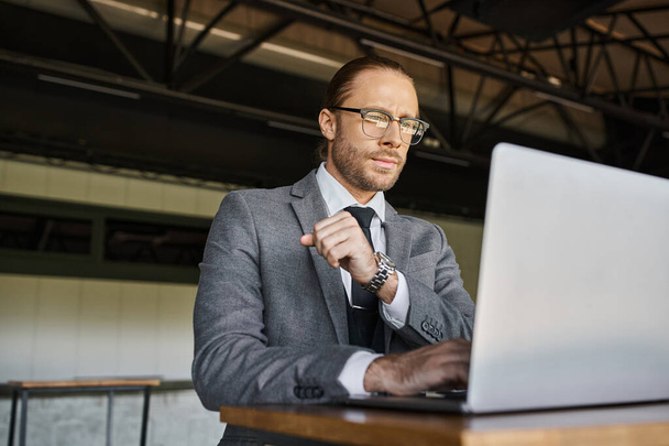 atractivo hombre refinado en traje inteligente gris con gafas y corbata de trabajo en el ordenador portátil, concepto de negocio - Foto, imagen