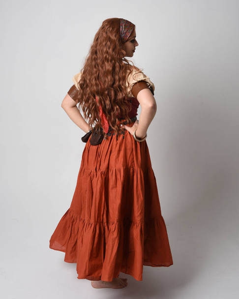 中世の乙女を着た美しい赤毛の女性の完全な長さの肖像画,フォーチュン・テラーの衣装. 立ち止まって,歩いて戻ってくる. スタジオの背景に隔離された. - 写真・画像