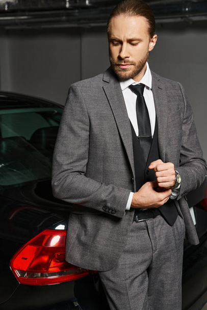 όμορφος κομψός επιχειρηματίας με κόκκινα μαλλιά σε έξυπνη στολή που ποζάρει δίπλα στο αυτοκίνητό του στο πάρκινγκ - Φωτογραφία, εικόνα