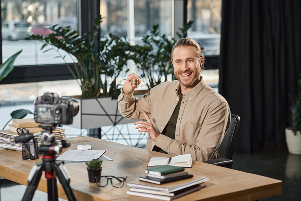χαρούμενος επιχειρηματίας που δείχνει bitcoins και καταγραφή βίντεο blog στην ψηφιακή φωτογραφική μηχανή στο γραφείο - Φωτογραφία, εικόνα